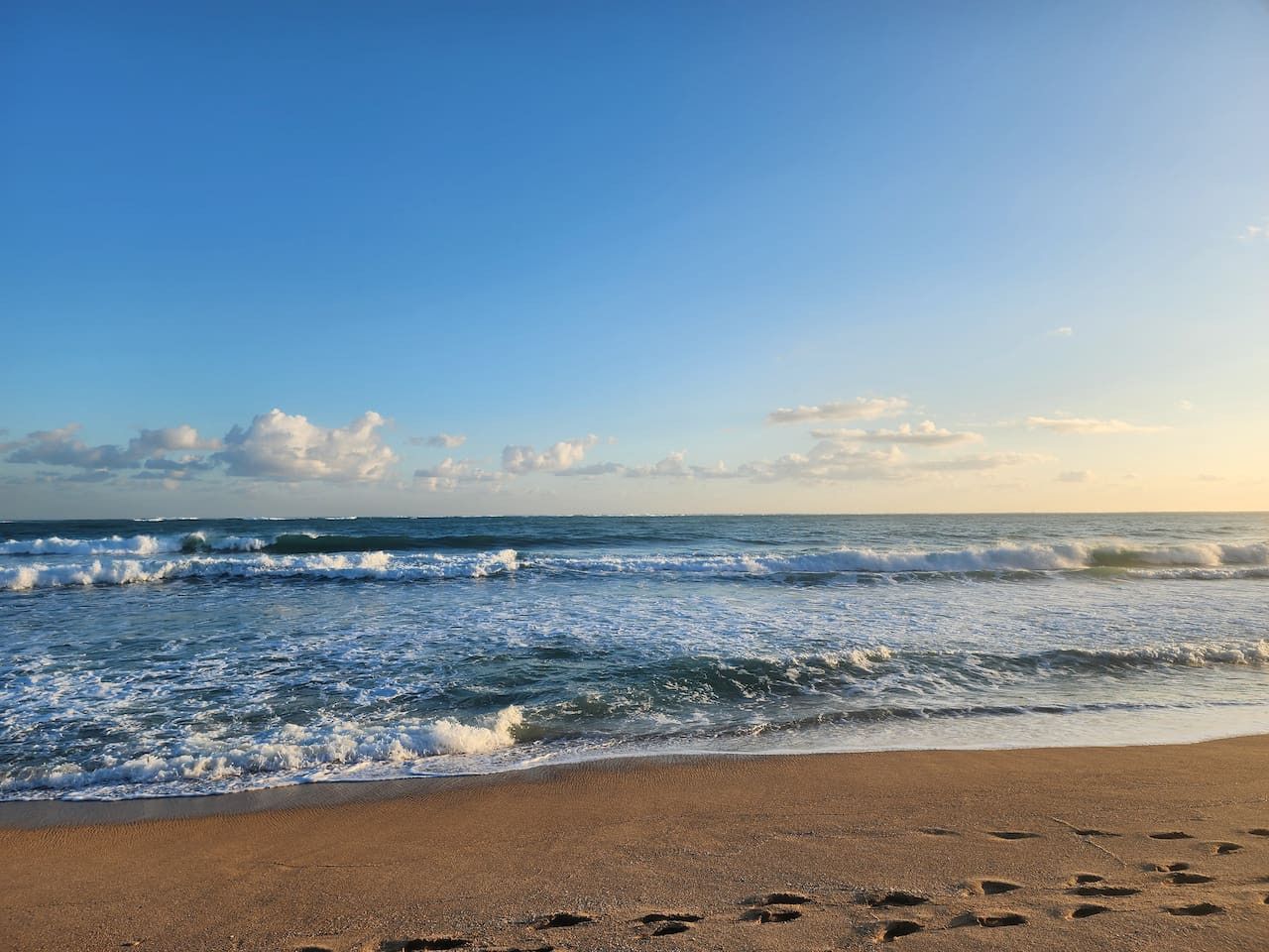 Een strand met golven, voetafdrukken en een heldere lucht.