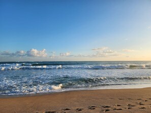 Una playa con olas, huellas en la arena y cielo despejado.