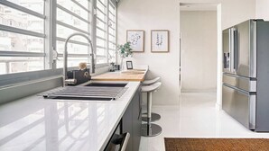 Una cocina moderna con un refrigerador de acero inoxidable, un ventanal con vistas a edificios y un lavamanos con un grifo moderno.