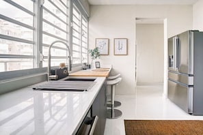 Una cocina moderna con un refrigerador de acero inoxidable, un lavamanos con grifo y una ventana con vista a un paisaje urbano.