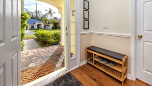 Un pasillo con un banco de madera, una puerta y vistas a una casa y jardín.