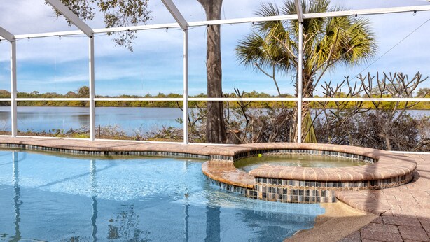 Una piscina con borde curvo, rodeada por una terraza de ladrillo y una estructura de pérgola blanca.