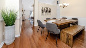 Un comedor con mesa y sillas de madera, una planta grande en maceta y una obra de arte en la pared.