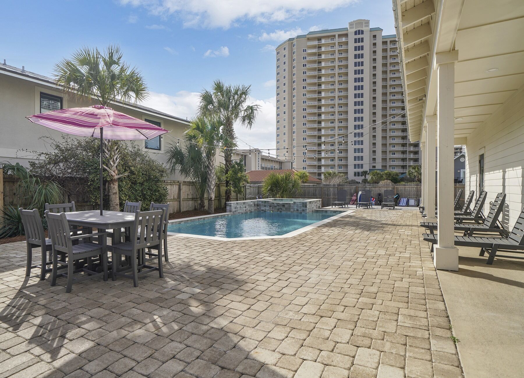 A pool area with a table and chairs, surrounded by palm trees and a tall building in the background.