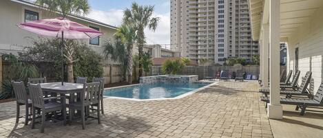 A pool area with a table and chairs, surrounded by palm trees and a tall building in the background.