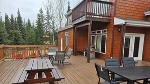 A wooden deck with outdoor furniture, a grill, and a covered area with a railing.