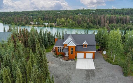 A two-story house with a garage, surrounded by dense forest and a lake.