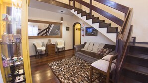 A staircase with wooden railings leading to an upper floor, a living room with a sofa, chairs, and a patterned rug. - Pousada Green House by Conrado Vitali (Canela)