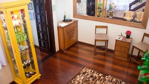 A room with wooden flooring, a yellow cabinet with bottles, a wooden desk, a chair, and a small table with a vase. - Pousada Green House by Conrado Vitali (Canela)