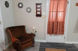 Enter a warm and inviting space with a classic armchair, elegant vase, and a welcoming doormat.