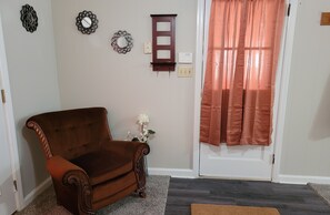 Enter a warm and inviting space with a classic armchair, elegant vase, and a welcoming doormat.