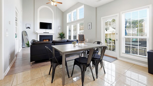 Un salon spacieux avec une cheminée, une table à manger avec des chaises et une grande fenêtre équipée de stores.