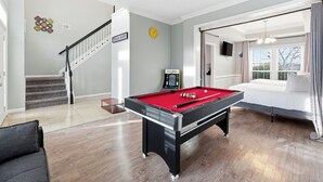 Une pièce avec une table de billard, un lit, un escalier et une vue sur l’extérieur.