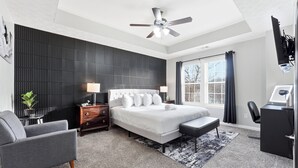 Une chambre moderne comprenant un lit, des tables de chevet, un bureau, une chaise, un ventilateur de plafond et une fenêtre avec des rideaux.