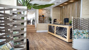 Zona de recepción con un mostrador de madera, una planta y una escalera que sube a un nivel superior.