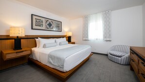 Una habitación de hotel moderna con una cama grande, lámparas de noche, una mesita de madera, una silla y un ventanal con cortinas.