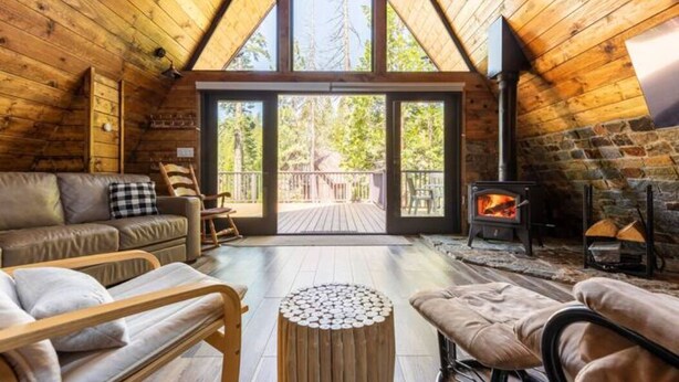Interior acogedor de una cabaña con techo de madera, chimenea, sofá y vistas a través de puertas de cristal.