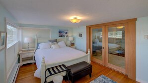 A bedroom with a large bed, bedside tables, a bench, a window, and a sliding glass door leading to a bathroom. - Albatross Landing on the beach approach (Ocean Park)