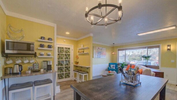 A kitchen with a microwave, coffee maker, and a chandelier. There is a dining table with a vase of utensils. - Albatross Landing on the beach approach (Ocean Park)