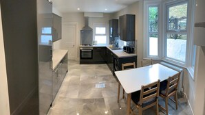 A modern kitchen with a central island, a dining area with a table and chairs, and a large window providing a view of the outdoors. - The Dimmer. 2 Bedroom Apartment (London)