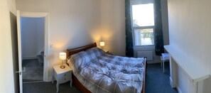 A bedroom with a bed, two bedside tables with lamps, a window with curtains, and a radiator. - The Dimmer. 2 Bedroom Apartment (London)