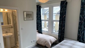 A bedroom with two beds, a window with curtains, a bedside table, and a mirror. - The Dimmer. 2 Bedroom Apartment (London)