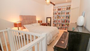 A bedroom with a bed, bedside lamps, a bookshelf, and a piano. - 2 The Reformed Church (Alnwick)