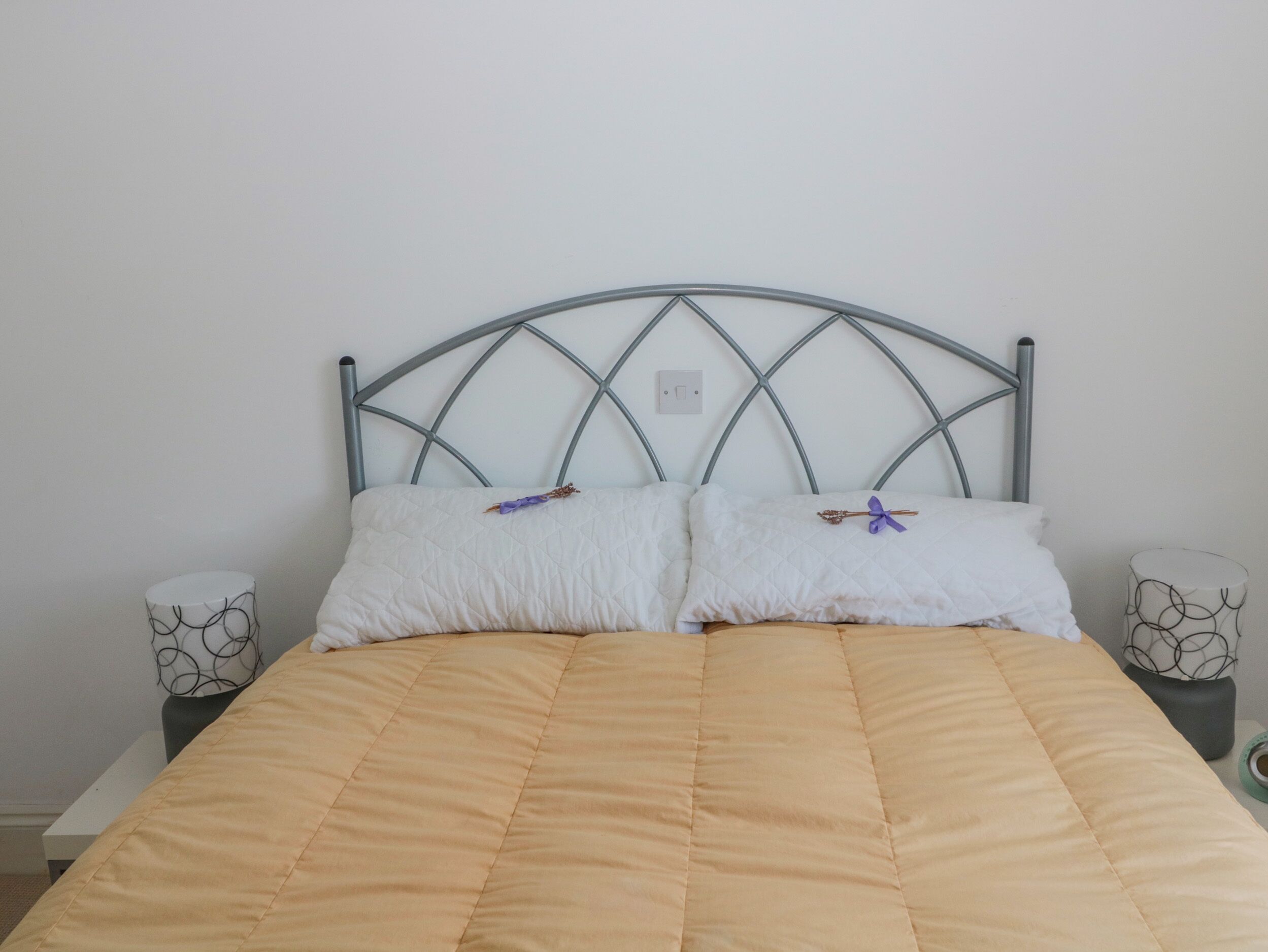 Un lit avec une tête de lit en métal, deux oreillers et une couvre-lit beige.