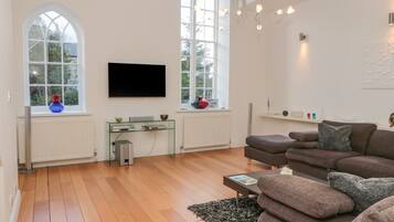 A modern living room with a large flat-screen TV, a glass coffee table, and a brown sofa.