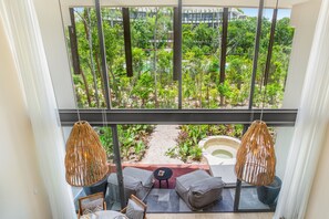 A balcony with a view of a lush garden, two wicker pendant lights, and a seating area with cushions and a small table. - Mistiq Temple I (Tulum)