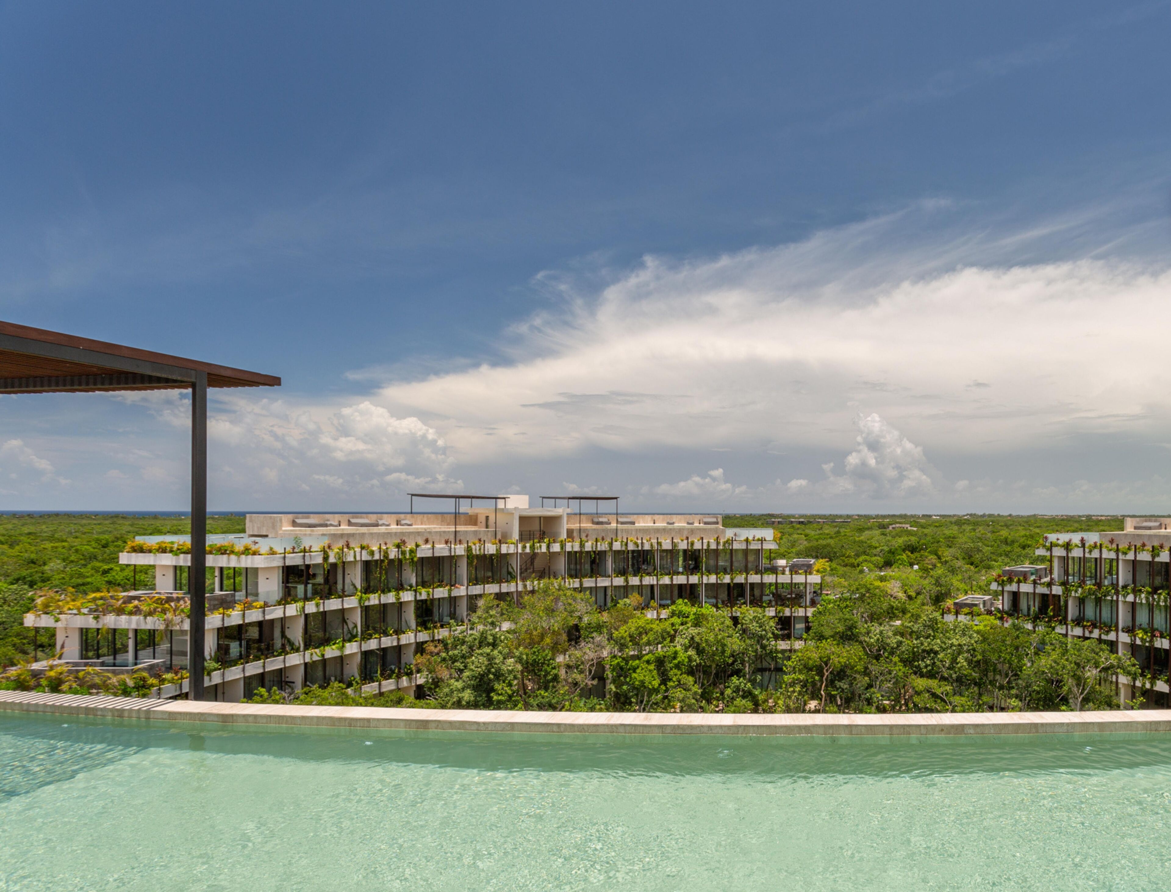 A modern resort with a pool, lush greenery, and a clear sky.