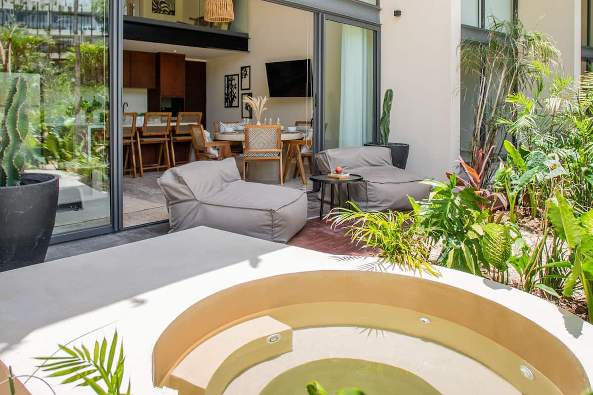 Un espacio exterior moderno con piscina, mobiliario para sentarse y abundante vegetación.