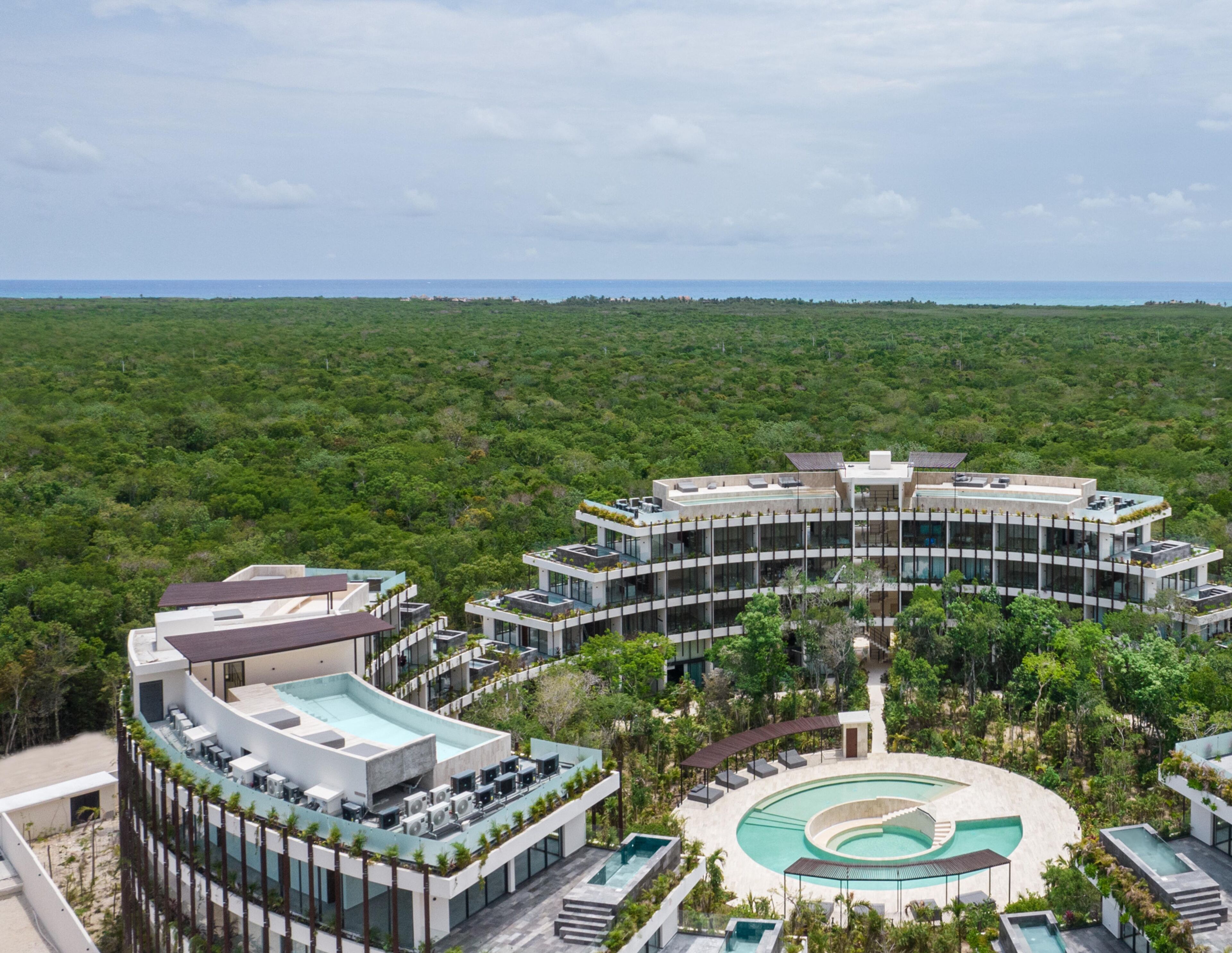 Un complexe hôtelier moderne doté d’une piscine centrale circulaire, de plusieurs étages réservés aux clients et d’une végétation luxuriante.