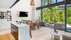 Cozinha moderna com ilha central, área de jantar com cadeiras de madeira e grandes janelas com vista para um jardim exuberante.