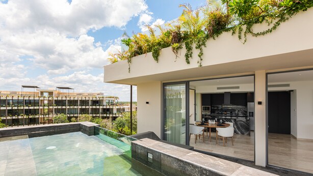 Uma área moderna de piscina ao ar livre, com um espaço de refeições envidraçado e cozinha visível através das portas de vidro.