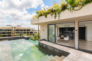 A modern outdoor pool area with a glass-enclosed dining space and a kitchen visible through the glass doors. - Mistiq Temple I (Tulum)