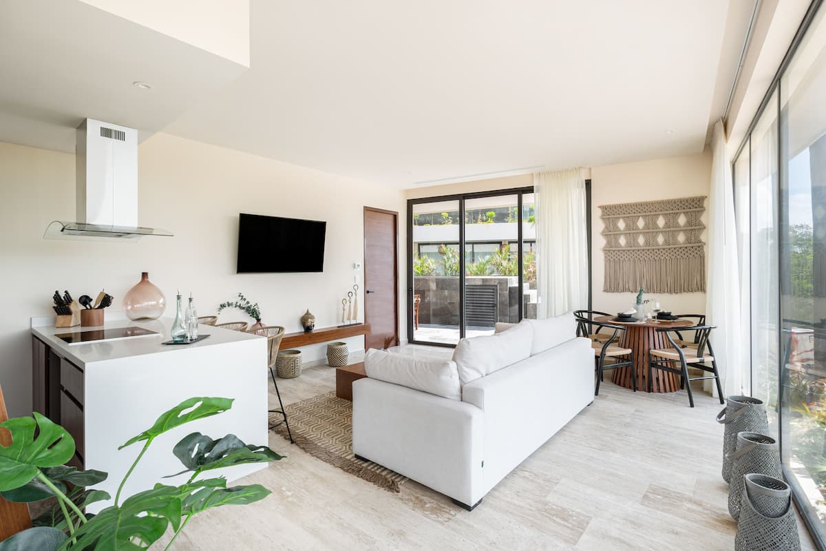 Una sala de estar moderna con un sofá blanco, un comedor con una mesa redonda y una cocina con encimera blanca y estufa empotrada.