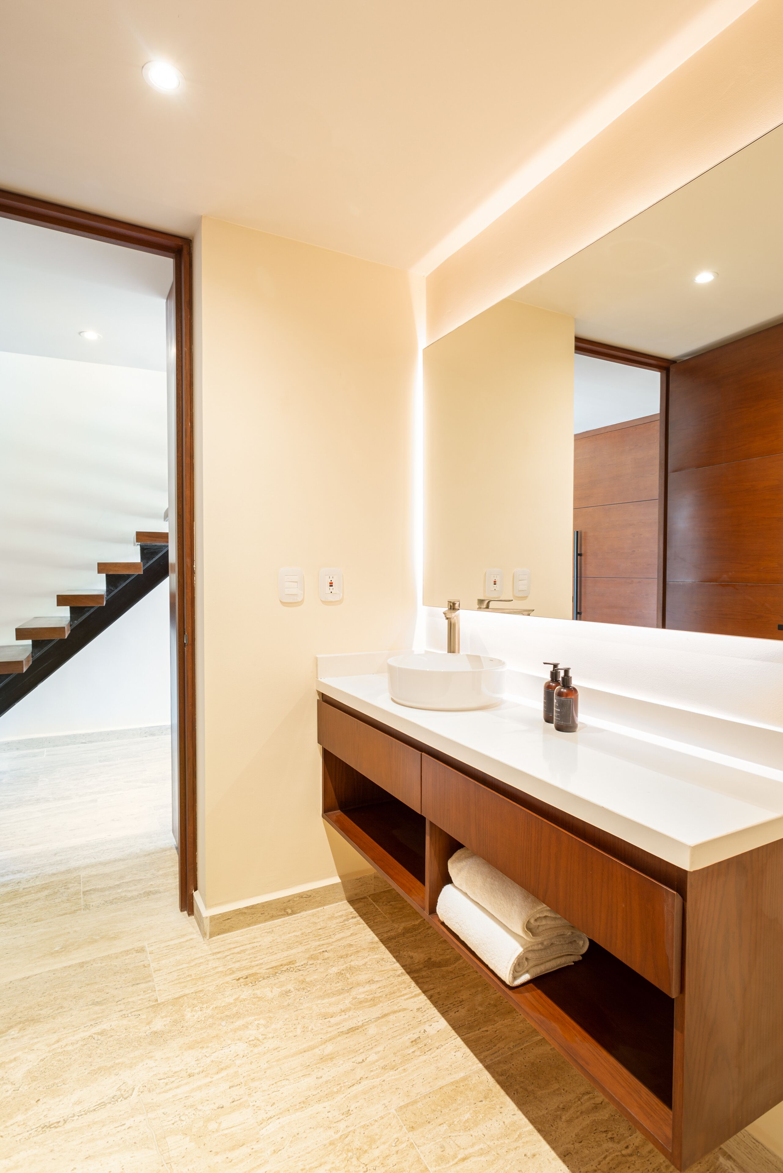 Un baño moderno con lavamanos blanco, tocador de madera y un espejo grande.