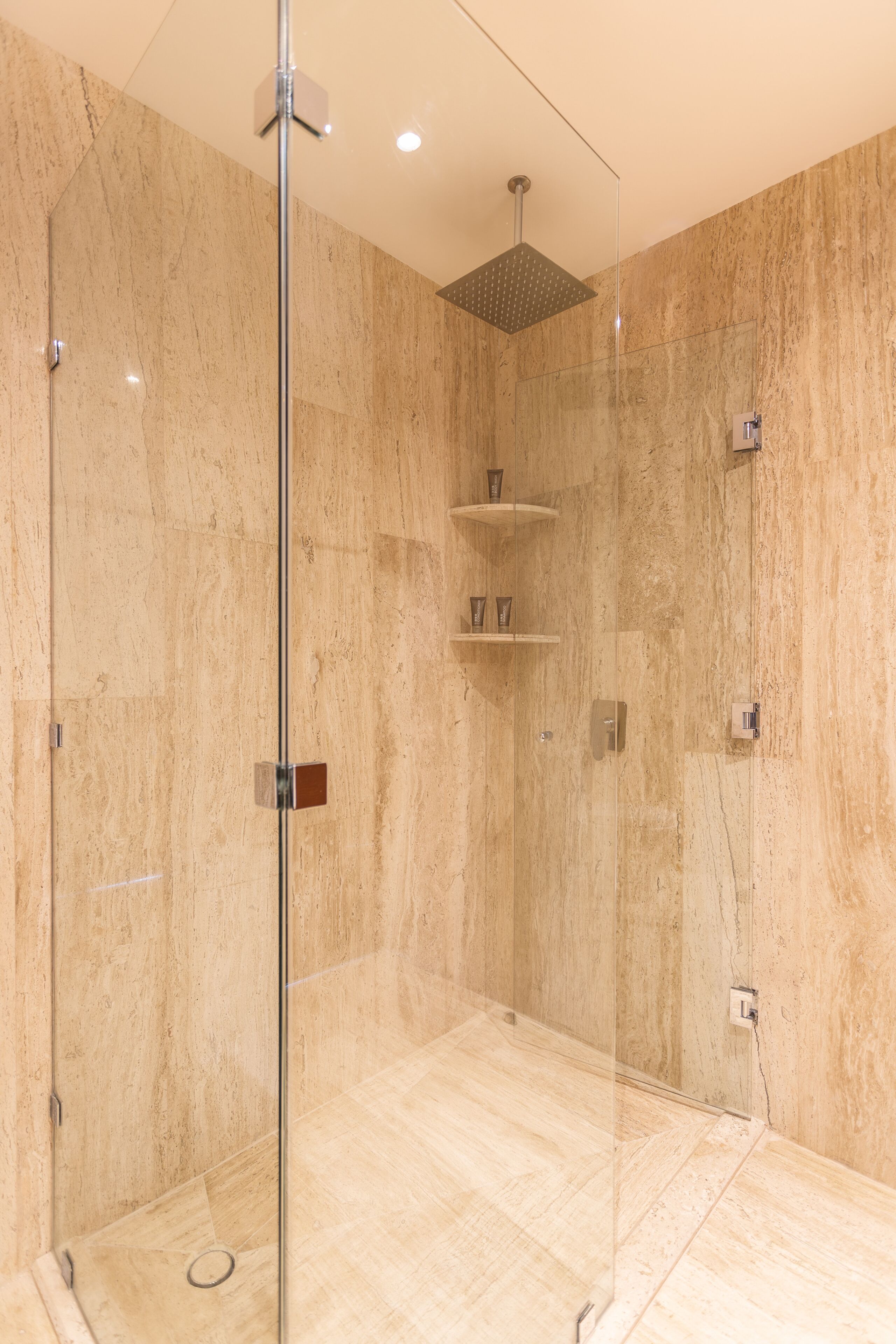 Eine moderne Dusche mit Glastür, Marmorwänden und einer an der Decke befestigten Duschbrause.