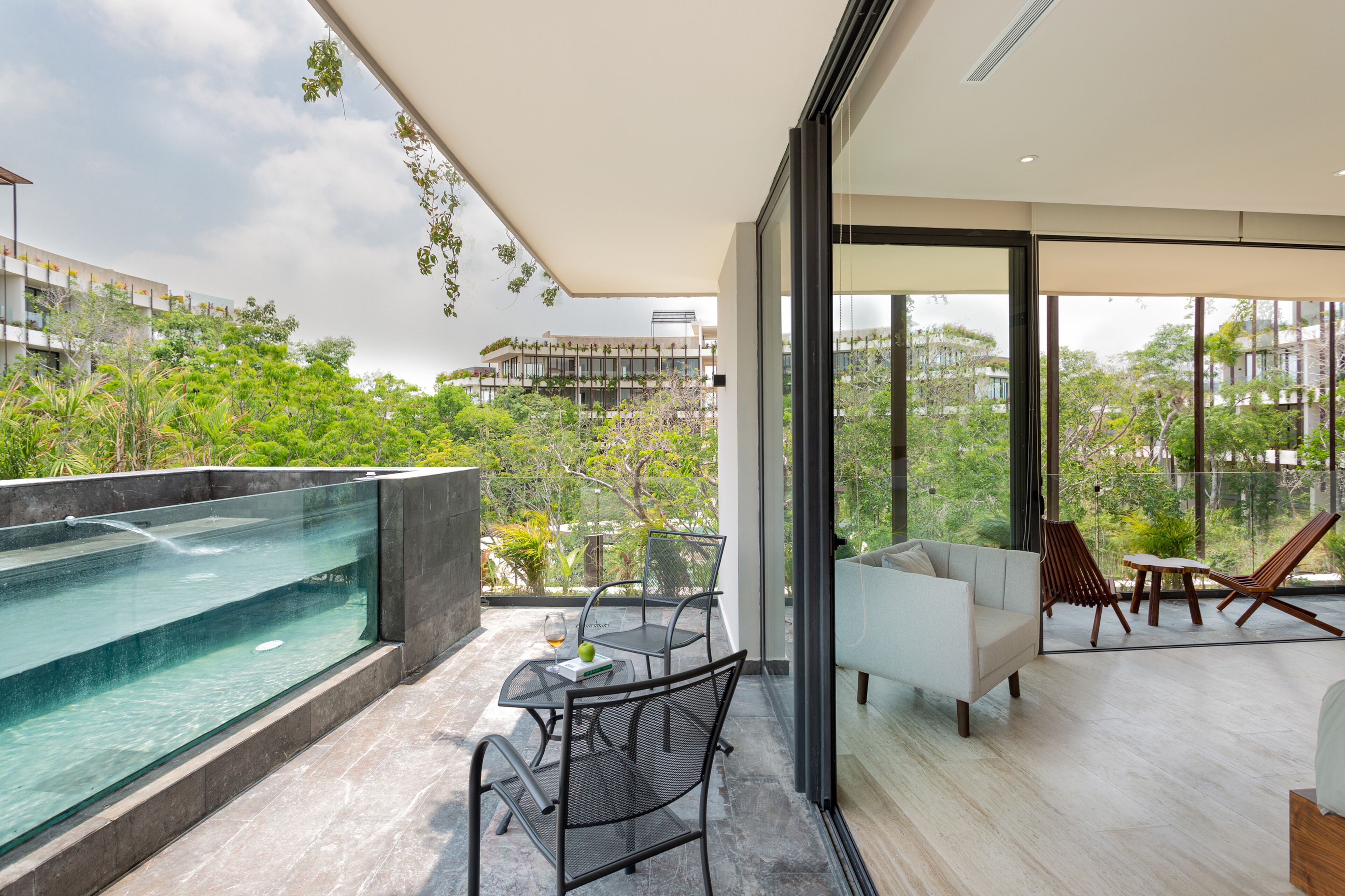 A modern balcony with a glass barrier, a pool, and a seating area with a sofa and chairs.