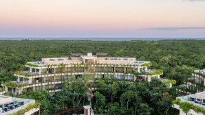 Um resort moderno com piscina central, rodeado por vegetação exuberante e vários edifícios.