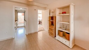 Un pasillo amplio con piso de madera, un mueble blanco con estantes y una lámpara colgante.