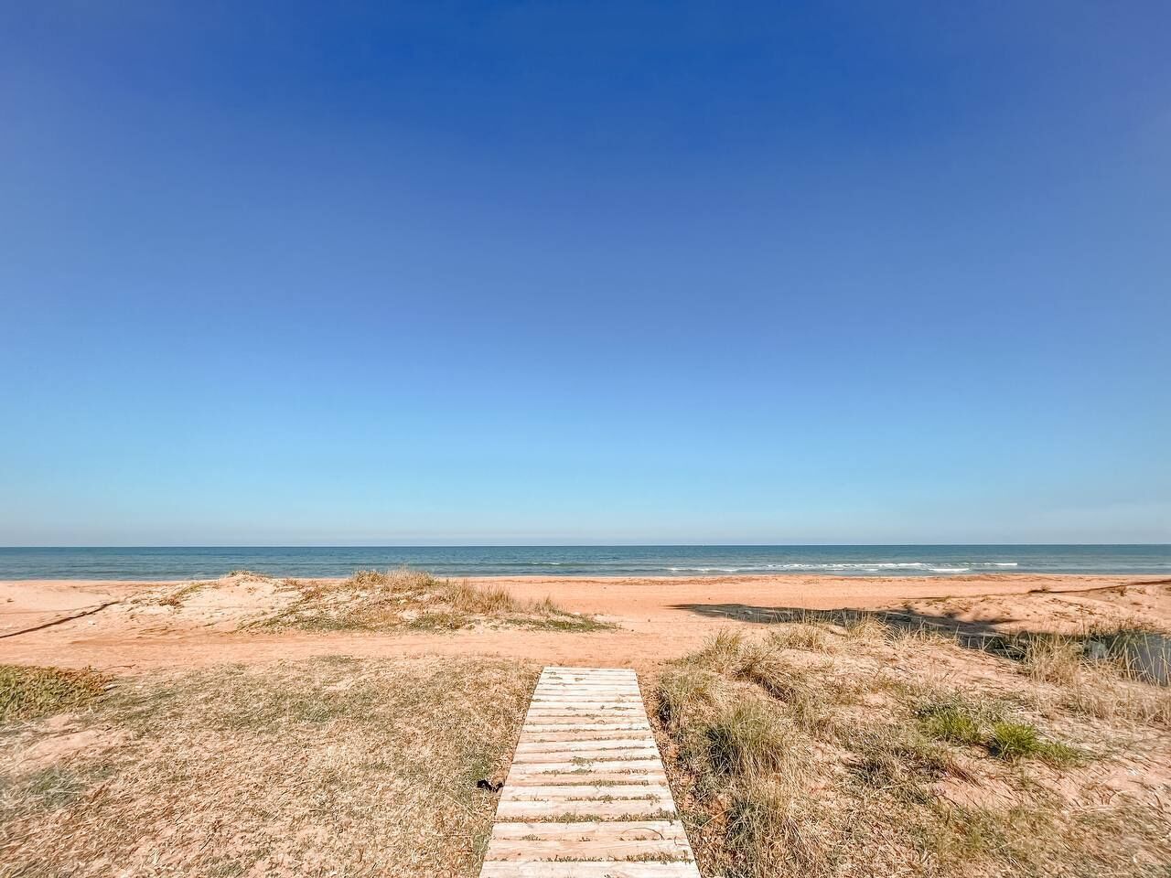 Un sendero de madera que conduce a una playa con cielos despejados.