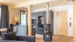 A modern kitchen with stainless steel appliances, a central wood-burning stove, and a dining area with a sofa and table. - Chalet  with 4 bedrooms & wellness (Biberwier)