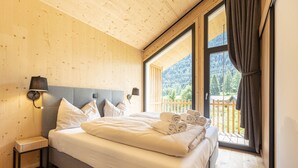 A bedroom with a large bed, wooden walls, a nightstand, and a view of a balcony with a wooden railing. - Chalet  with 4 bedrooms & wellness (Biberwier)