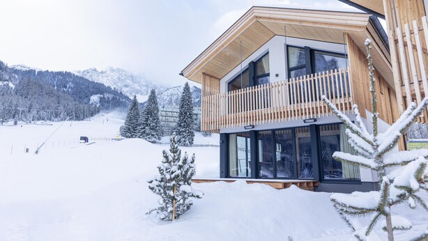 A modern chalet with a wooden balcony, large windows, and a view of a snowy mountain landscape. - Chalet  with 4 bedrooms & wellness (Biberwier)