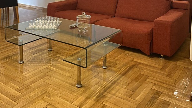 Una sala de estar con una mesa de centro de vidrio, un sofá rojo, piso de madera y un espejo grande.