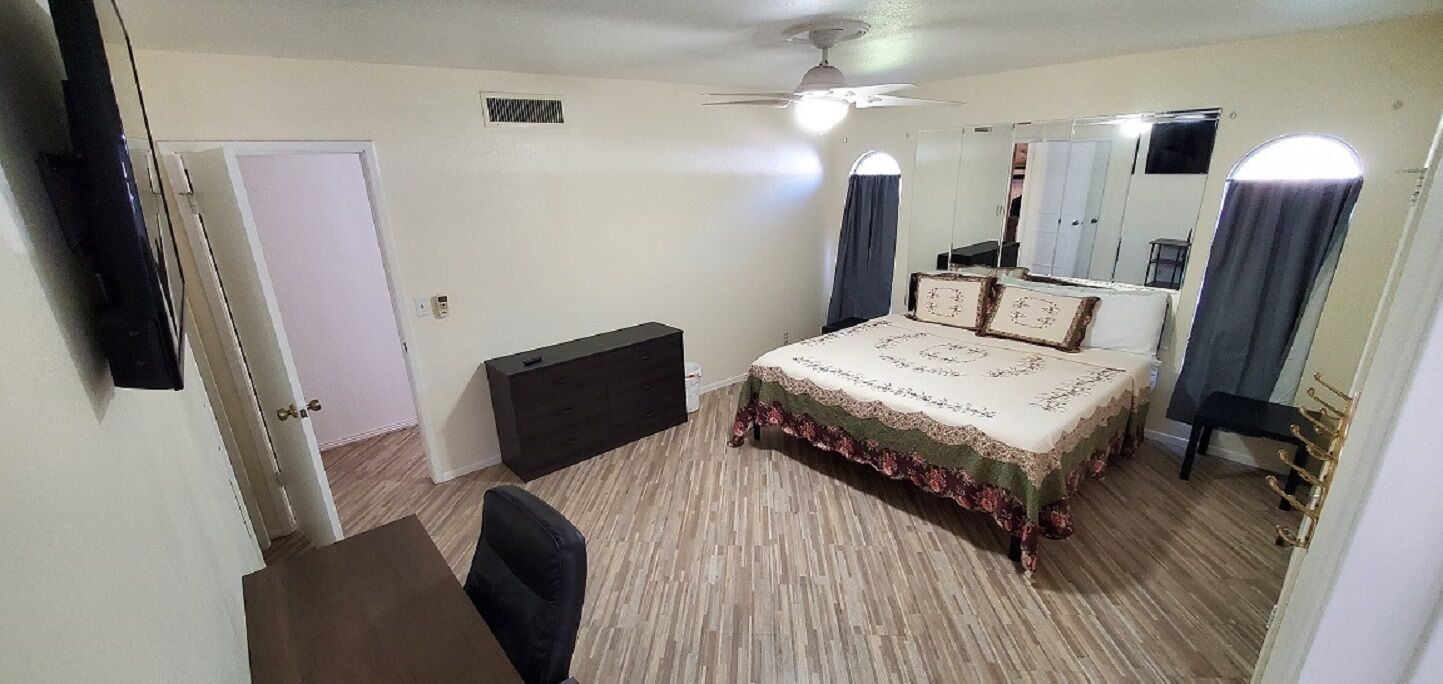 A bedroom with a bed, a desk, a chair, a wardrobe, and a ceiling fan.