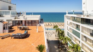Une terrasse sur le toit avec des sièges extérieurs, une piscine et une vue sur la plage et l’océan.