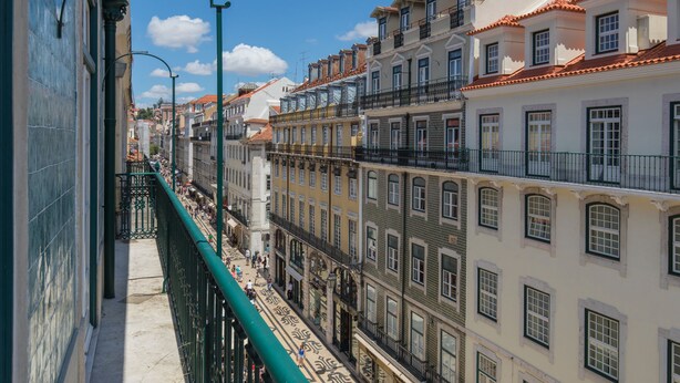 Una calle estrecha flanqueada por edificios, con balcones y una barandilla de metal verde.